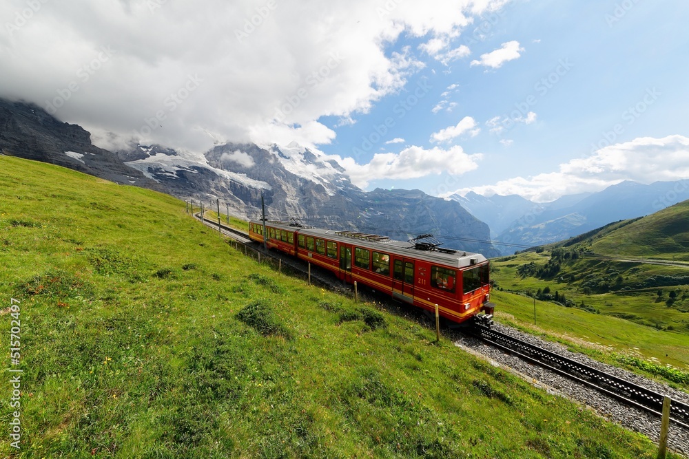 A cog-wheel train travels on famous Jungfrau Railway from Kleine Scheidegg to Jungfraujoch station ( top of Europe ) on the green grassy hillside, in Berner Oberland ( Bernese Highlands ), Switzerland