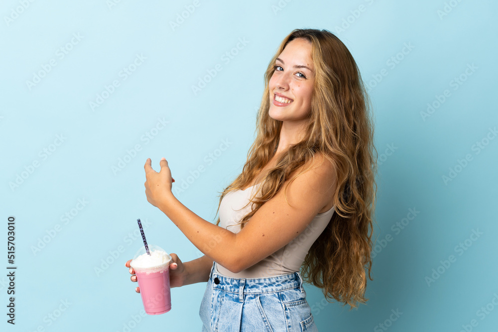 Young woman with strawberry milkshake isolated on blue background pointing back Young woman with strawberry milkshake isolated on blue background pointing back