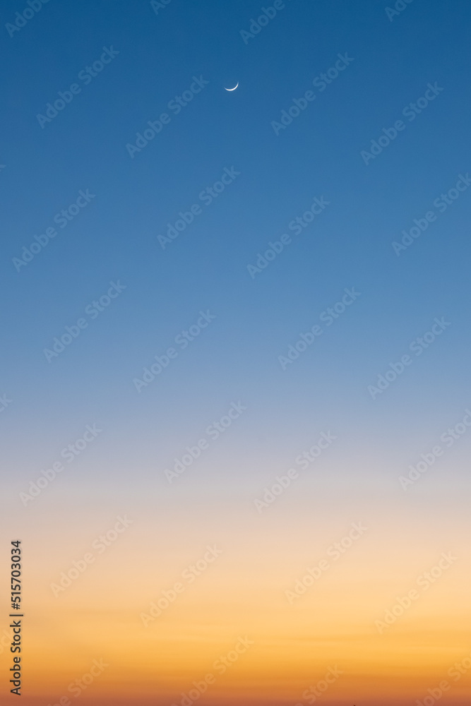 Clear blue and orange sunset sky with crescent moon.