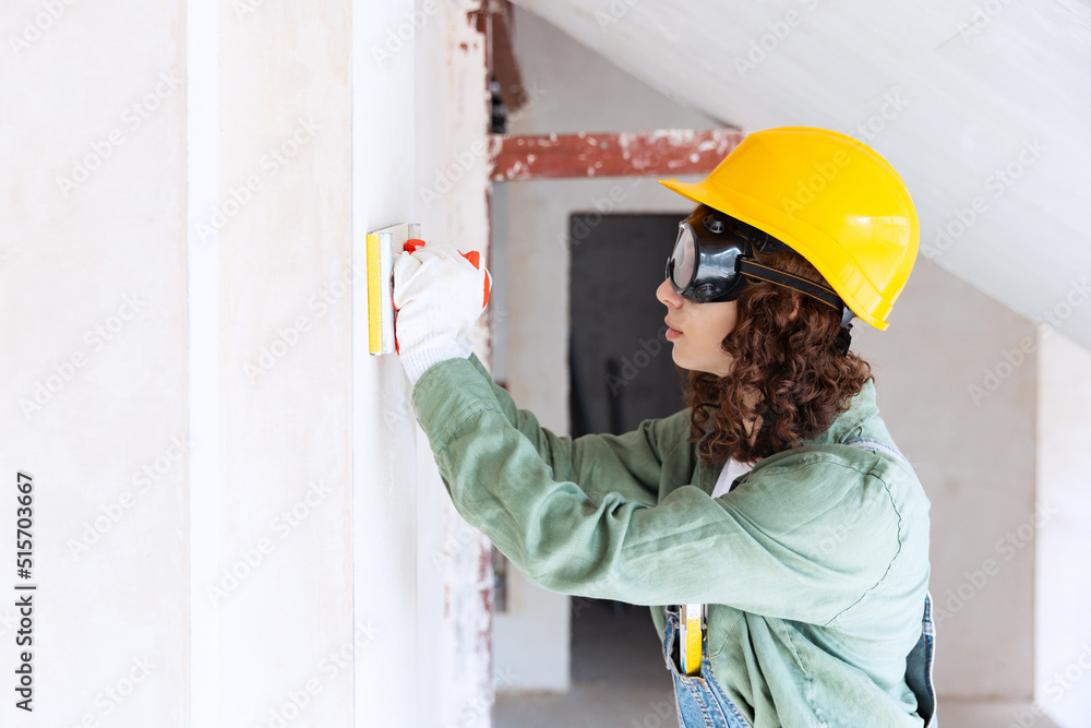 Live portrait of young woman, builder wearing helmet using different work tools at a construction site. Gender equality, job, work concept Live portrait of young woman, builder wearing helmet using different work tools at a construction site. Gender equality, job, work concept