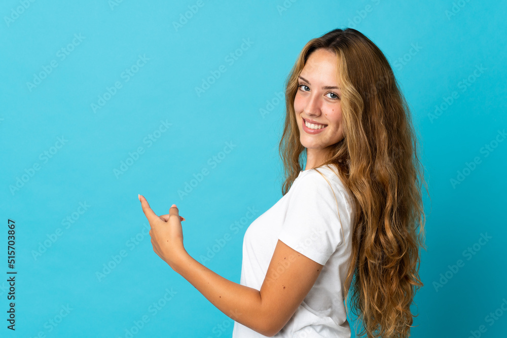 Fototapeta premium Young blonde woman isolated on blue background pointing back
