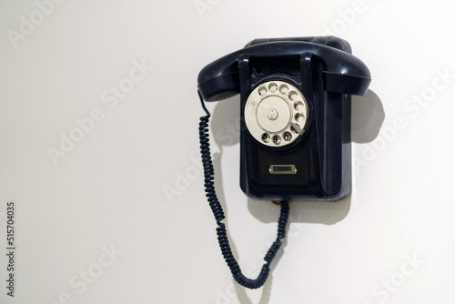 An old black analog phone made of ebony hangs on the wall