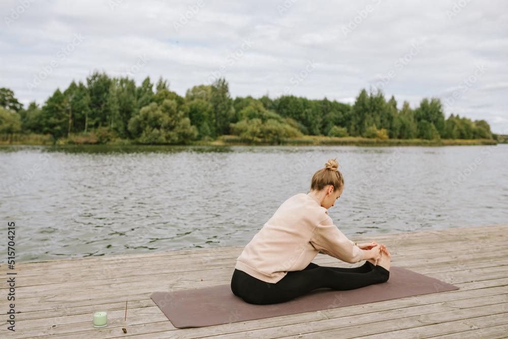 Young woman doing yoga by the water. Fitness, wellness, soul-searching concept.