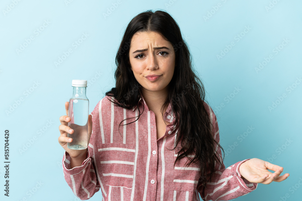 Young woman with a water isolated on blue background making doubts gesture while lifting the shoulders Young woman with a water isolated on blue background making doubts gesture while lifting the shoulders