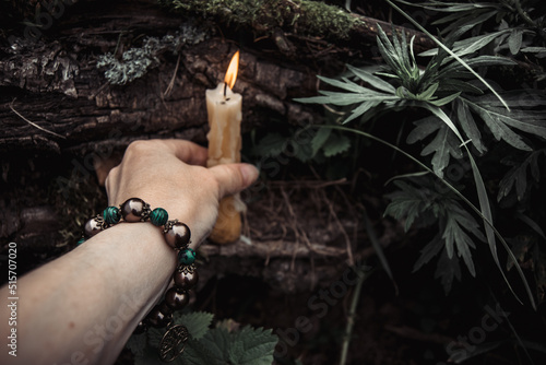 burning candles and a womans hand with a bracelet on a dark natural background. pagan wiccan, slavic traditions. Witchcraft, esoteric spiritual ritual for mabon, halloween, samhain. 