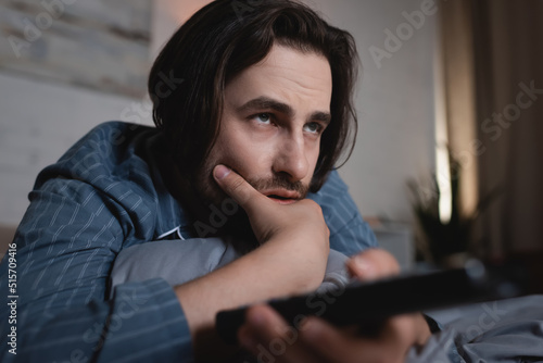 Young sleepless man with remote controller watching film on bed © LIGHTFIELD STUDIOS