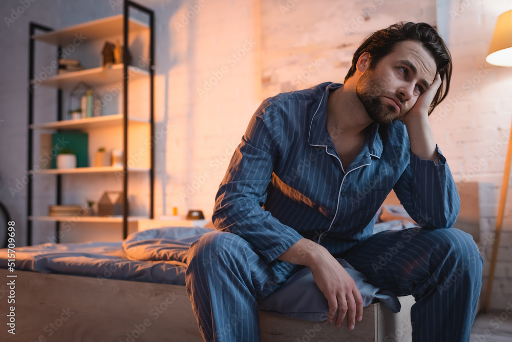 Tired man in pajama sitting on bed at night Tired man in pajama sitting on bed at night