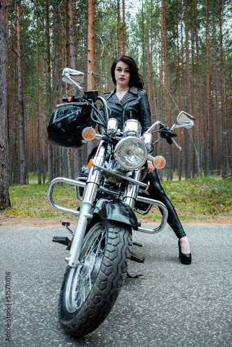A girl in tight black leather sits on a motorcycle.