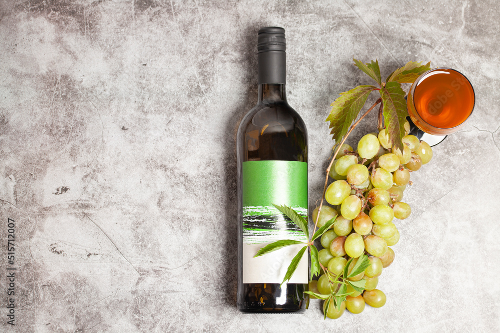 Obraz premium White wine bottle with bunch of grapes, glass on a dark background, top view.