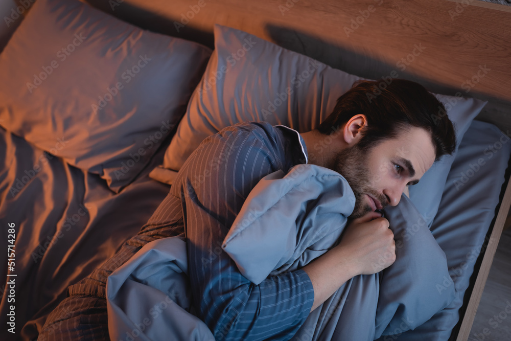 Top view of man in pajamas suffering from insomnia on bed at night Top view of man in pajamas suffering from insomnia on bed at night
