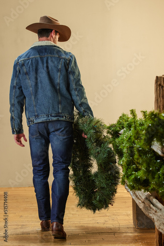 cowboy walking with wreath along a fence wrapped in Christmas decorations Fototapeta
