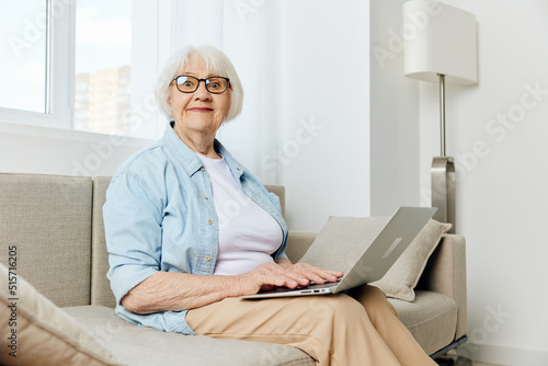 a pleasant emotional elderly pensioner is sitting on the couch with a laptop on her lap and emotionally looking at the camera