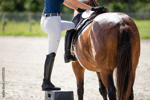 An equestrian mounts a horse from a mounting block.