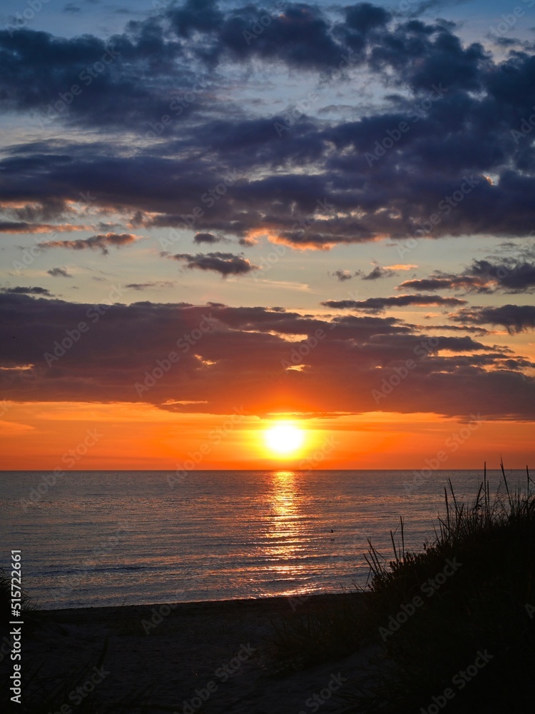 Naklejka premium Sunset into the ocean. Blue clouds contrast with orange sunrays.