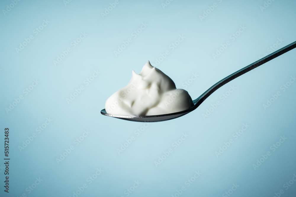 Sour cream in a spoon on a blue background - obrazy, fototapety, plakaty 