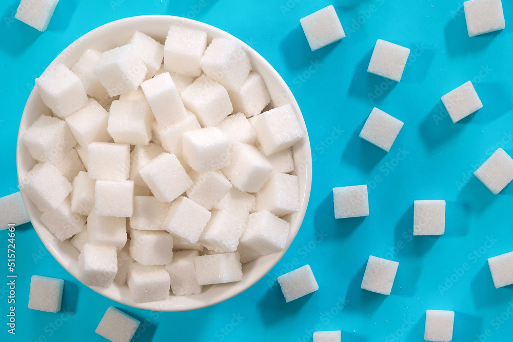 White sugar cubes in a bowl on a blue background. Refined cane sugar. White sugar cubes in a bowl on a blue background. Refined cane sugar.