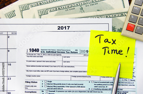 1040 US individual tax form, dollars, calculator, pen and yellow sticker on a wooden desc photo