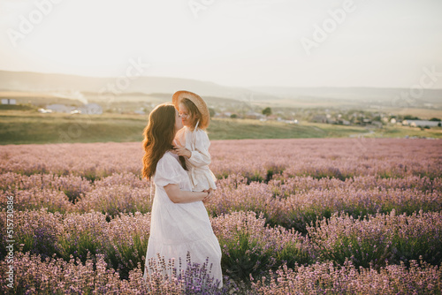 Happy mother and daughter wearing white vintage dresses having fun in lavender field at sunset.