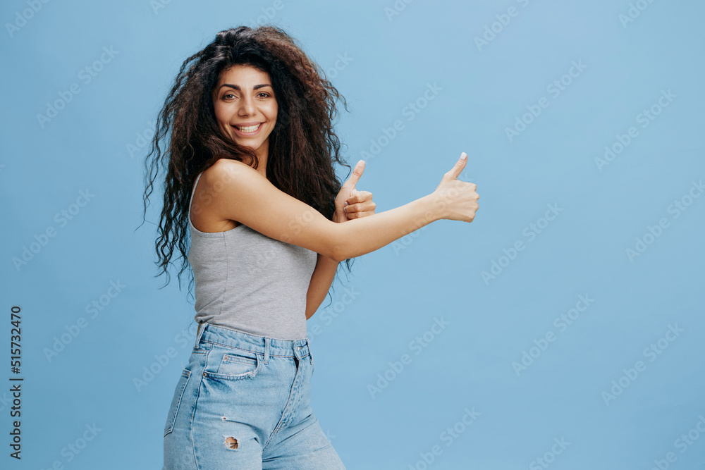 GREAT PURPOSE. Overjoyed beautiful Latin female with afro gesture thumbs up, look at camera. Fashion. Studio shoot over blue sky background. Copy space, free place for design ad GREAT PURPOSE. Overjoyed beautiful Latin female with afro gesture thumbs up, look at camera. Fashion. Studio shoot over blue sky background. Copy space, free place for design ad