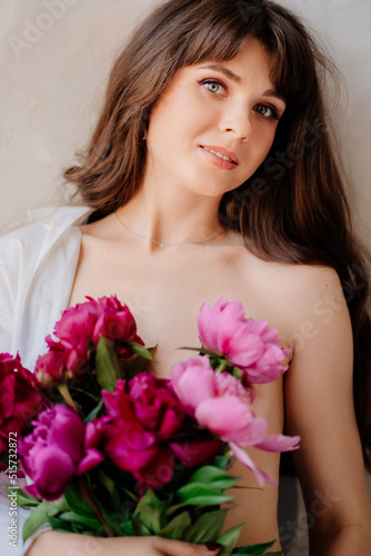 a woman topless wearing a white shirt on shoulder with a bouquet of peonies.