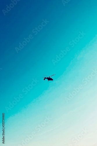 Silhouette of a helicopter in flight against a clear blue sky background.