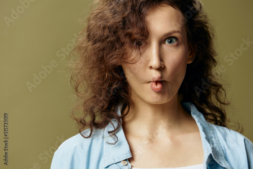 Funny cute curly beautiful female in jeans casual shirt makes lips bow like fish posing isolated on over olive green pastel background. Being Yourself. People Lifestyle emotions concept. Copy space