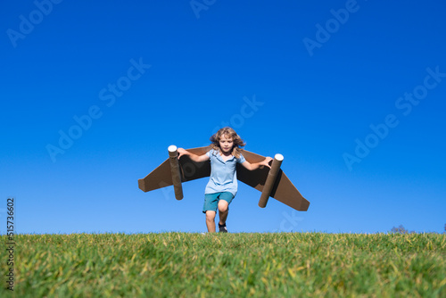 Little child plays astronaut or pilot. Child on the background of blue sky. Kids with paper wings jetpack dreams. Children imagines dreams of flying. Funny kid with toy jet pack. Success, imagination.