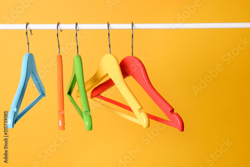 Bright clothes hangers on metal rail against yellow background