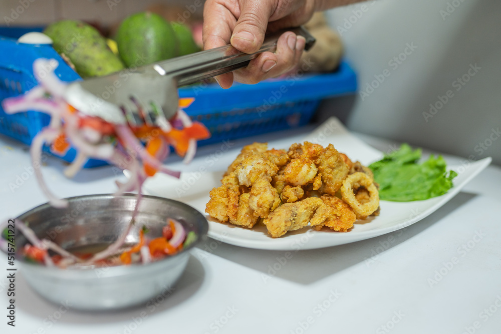 Cook plating ceviche in a dish with breaded meat and fish Cook plating ceviche in a dish with breaded meat and fish