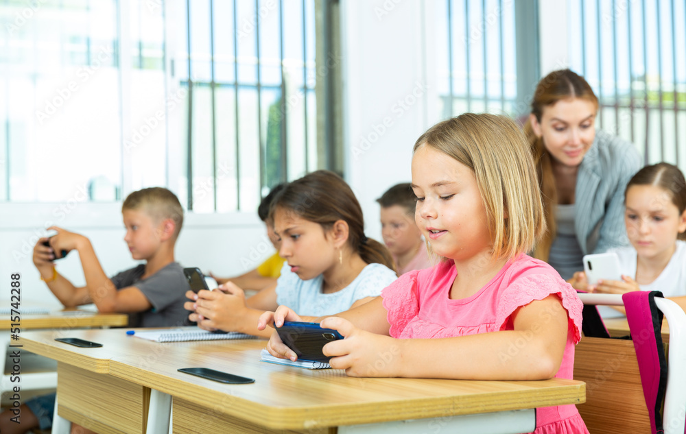 Fototapeta premium Group of schoolchilds using smartphones while working in classroom during lesson in primary school