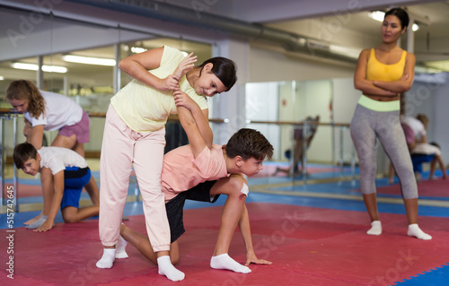 Sportive preteen kids practicing in pair self-protection in class with female teacher