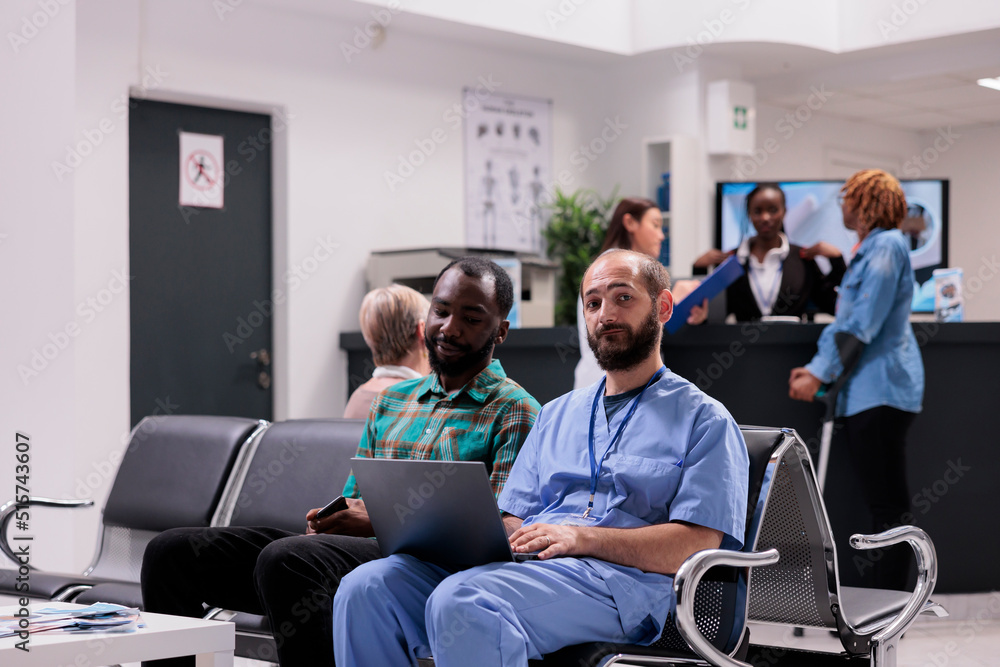 Medical nurse talking to male patient about diagnosis, showing disease results on laptop in hospital reception lobby. Specialist and sick person chatting about medicine in waiting room. Medical nurse talking to male patient about diagnosis, showing disease results on laptop in hospital reception lobby. Specialist and sick person chatting about medicine in waiting room.