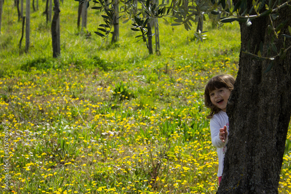 Picture of an adorable little girl hiding behind a tree in a flowery field. Picture of an adorable little girl hiding behind a tree in a flowery field.