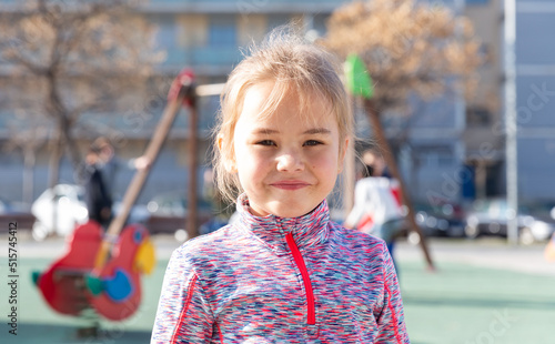 Portrait of small smiling girl standing on outdoors playground at sunny day
