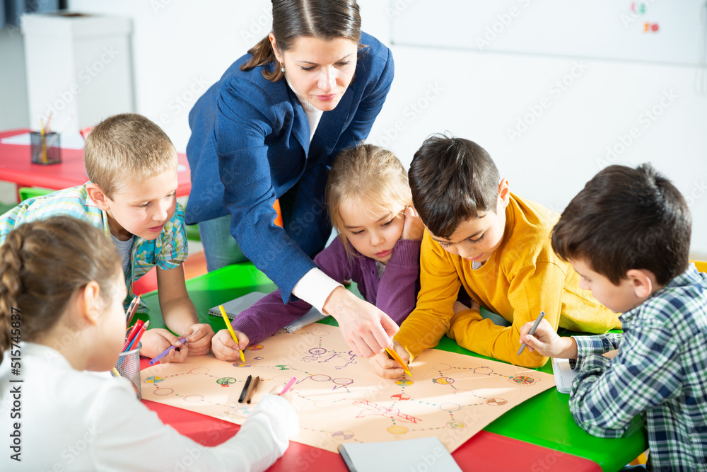 Group of school kids with teacher sitting together around desk in classroom, playing educational tabletop game