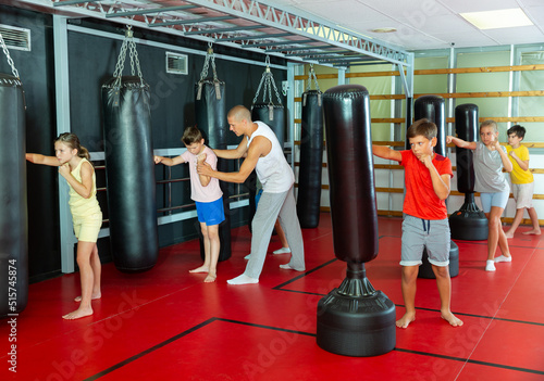 Group of kids boxing with punch bags during their group training. Trainer standing nearby and correcting them. © JackF