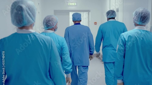 Back view of doctors wearing protective masks and uniform walking along the corridor in hospital operating block after successful surgical operation.