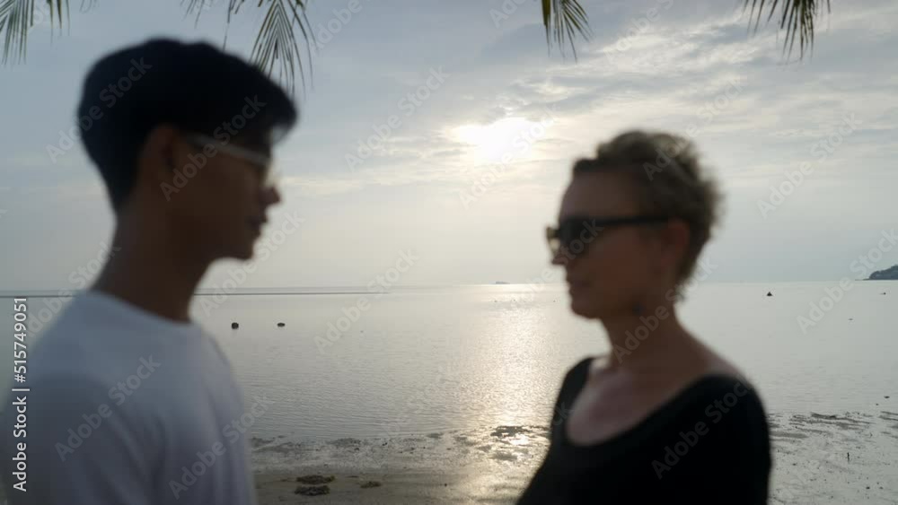Interracial couple with age differences kissing holding hands at sandy beach at sunset by the sea - slow motion unveil shot
