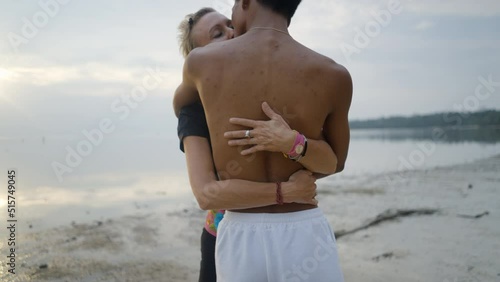 Interracial couple with age differences embrace and kissing on beach at sunset - push back slow motion