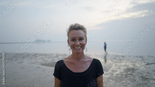 Middle-aged caucasian woman with short blond hair smiling standing at the beach at sunset - bust shot  photo