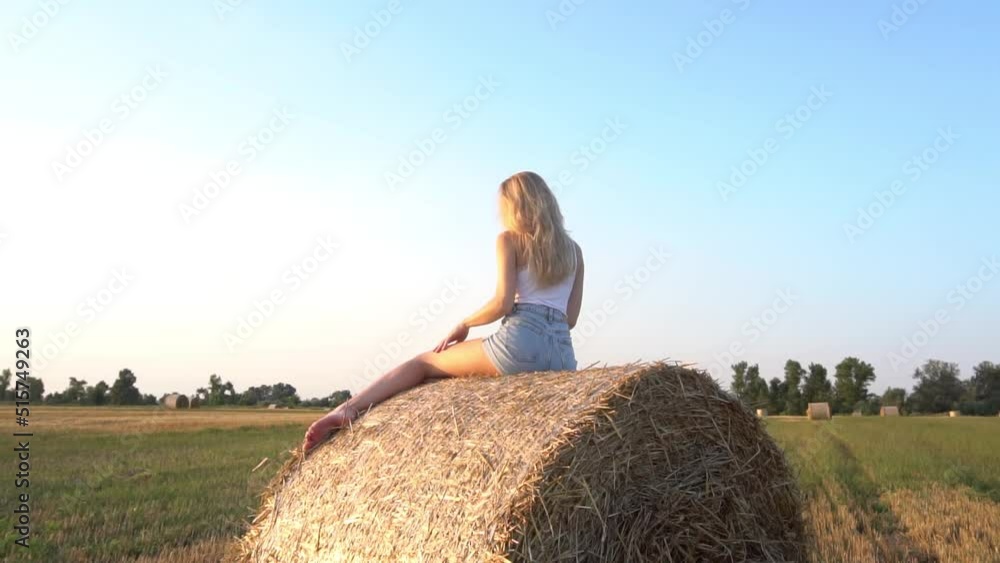 Slow Motion A happy young woman is sitting on a haystack in a mown field Slow Motion A happy young woman is sitting on a haystack in a mown field