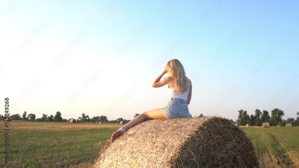An elegant, slender young girl with beautiful legs sits and rests on haystack An elegant, slender young girl with beautiful legs sits and rests on haystack