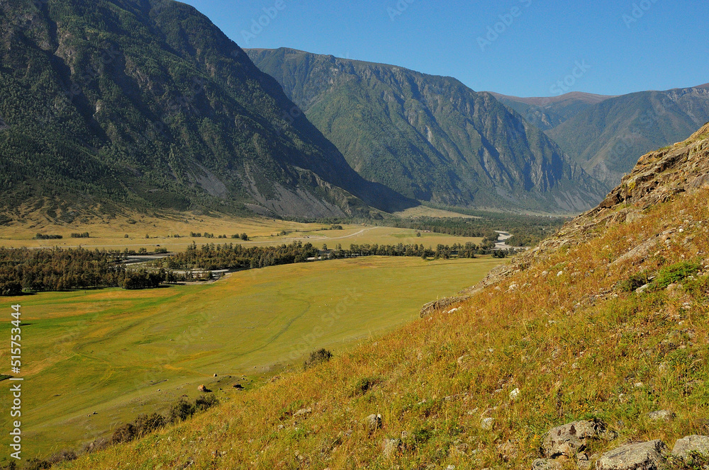 View from the top of the mountain to a narrow valley with fertile pastures and a flowing meandering river.