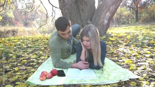 Happy young couple resting and reading book under the old tree in autumn park