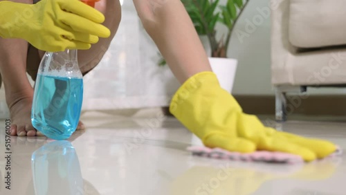 Asian woman wearing yellow rubber glover with cloth rag and detergent spray cleaning floor at home in living room, Female hands wash cleaner, housework and housekeeping concept photo