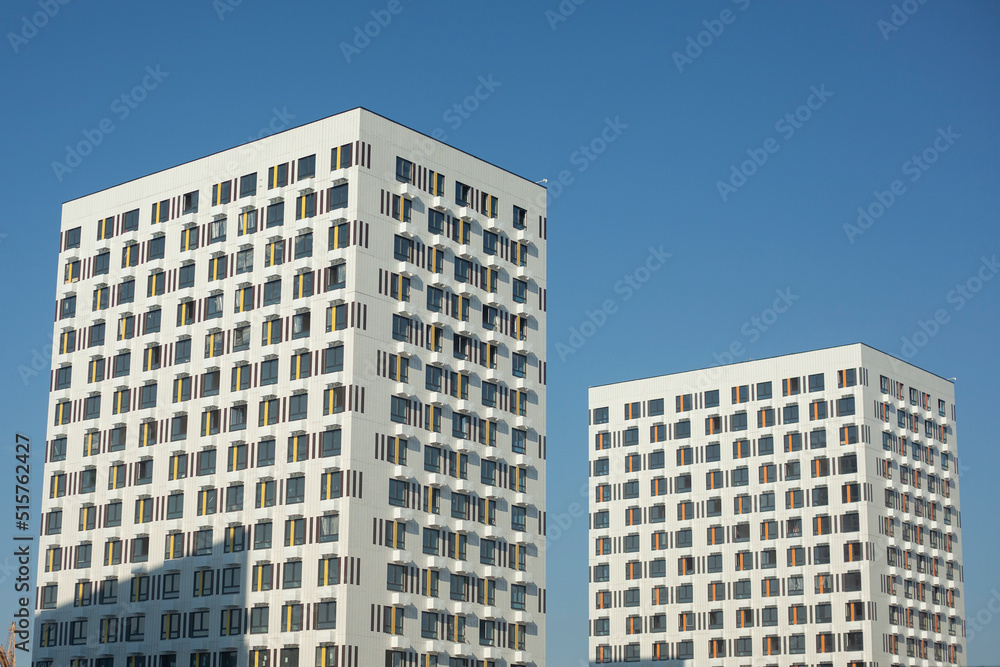 Two white buildings against blue sky. Two modern houses. View of city.