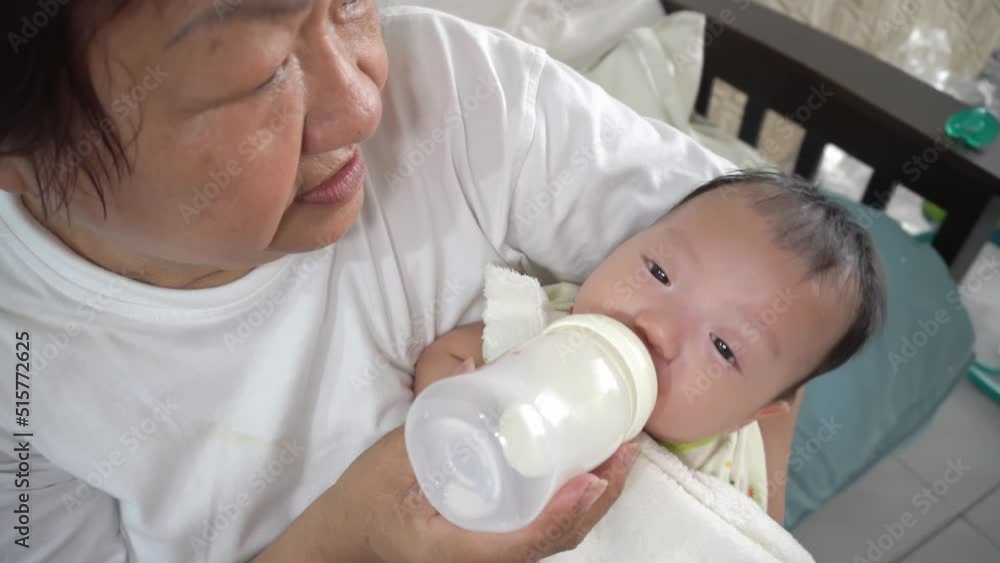 Chinese grandmother feed milk nutrition to baby boy at chair Chinese grandmother feed milk nutrition to baby boy at chair