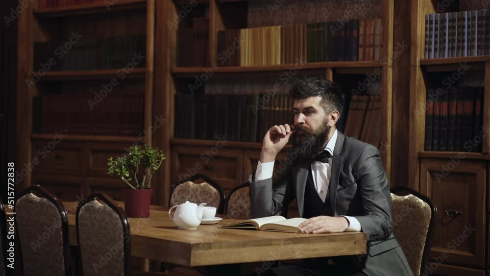 Professor reading book in classical library cabinet. Home library. Businessman sits in vintage interior, holds book and cup of tea. Business man in suit in his cabinet. Mature man enjoys reading. Professor reading book in classical library cabinet. Home library. Businessman sits in vintage interior, holds book and cup of tea. Business man in suit in his cabinet. Mature man enjoys reading.