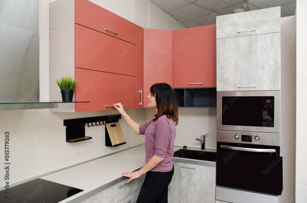 A young woman opens the kitchen cabinet door by the handle. A young woman opens the kitchen cabinet door by the handle.