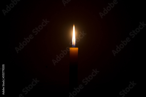 A single burning candle flame or light glowing on a Single small yellow candle is isolated on black or dark background on table in church or temple for Christmas, funeral or memorial service